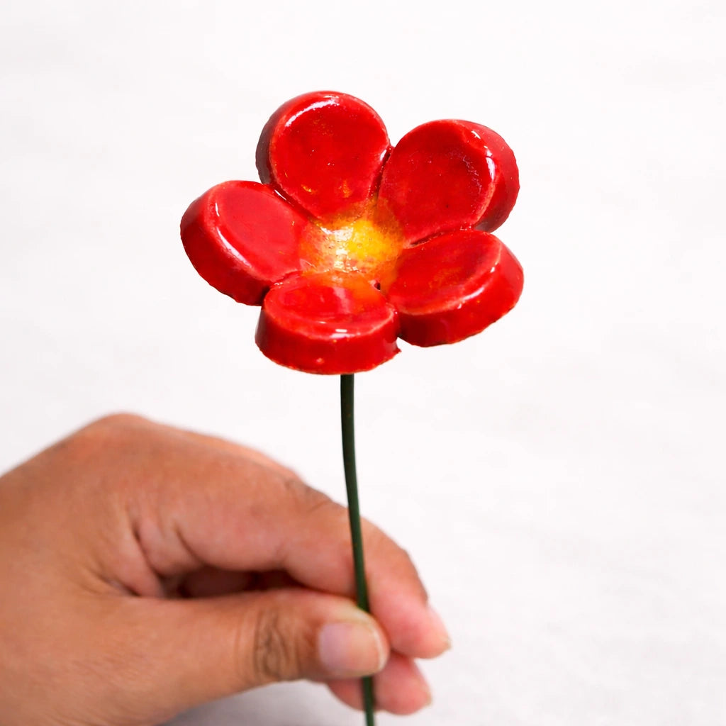 Handmade flower in bright red glaze with yellow center held by a hand, perfect for home decor or vase styling.